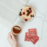 Chai Mate Tea Bags next to a cup of tea and pancakes topped with berries on a marble surface.