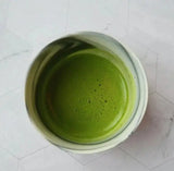 Green Matcha in a white cup on a light gray tiled surface