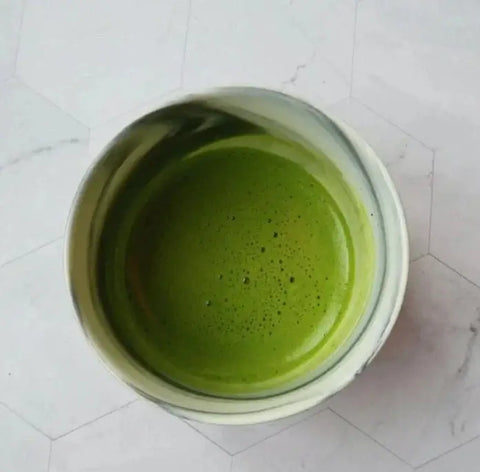 Green Matcha in a white cup on a light gray tiled surface