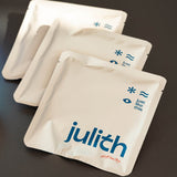 Three silver foil UFO Coffee Drip Bags sachets from the brand julith, arranged diagonally on a dark gray surface. The front sachet is clearly visible with the brand name 'julith' printed in blue, along with icons indicating 'Just Like This'.