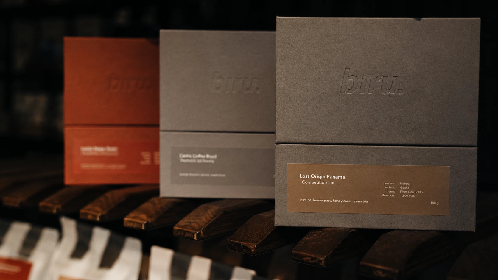 Three Bru· coffee product boxes arranged on a dark wooden surface, including a prominent taupe box labeled 'Lost Origin Panama' in the foreground, with a red box and other gray boxes behind it.
