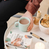 Person enjoying a cup of hot cocoa with Original Choc Blend chocolate and granola on a table.