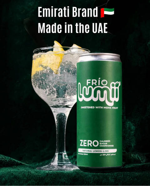 A green can of Frío Lumii Zero calories sparkling drink with lemon scent, shown next to a garnished cocktail glass on a dark green textured background. White text at the top reads 'Emirati Brand Made in the UAE' with a small UAE flag.