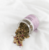 Ashwagandha + Chill Superfood Tea loose herbs spilling from a jar on a white background.
