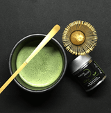 Pure Zen Premium Organic Japanese Matcha Green Tea Powder in a bowl with a bamboo whisk and matcha tin.