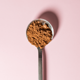 Classic Chocolate powder in a metal spoon against a pink background, highlighting its rich texture.