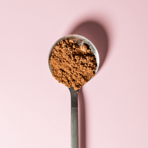 Classic Chocolate powder in a metal spoon against a pink background, highlighting its rich texture.