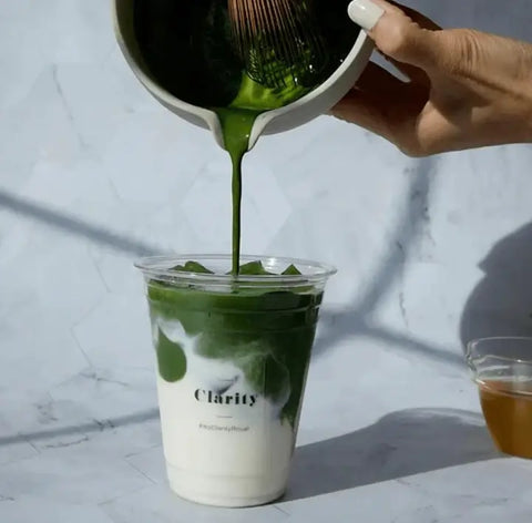Green Matcha being poured into a clear cup with a white lid on a light gray background