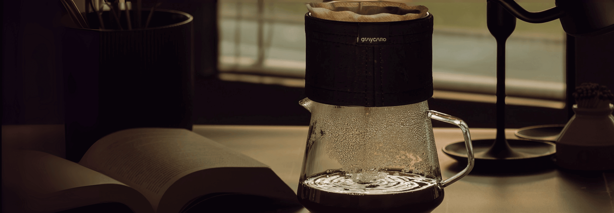 Pour-over coffee maker brewing on a desk beside an open book and a lamp, perfect for coffee enthusiasts.