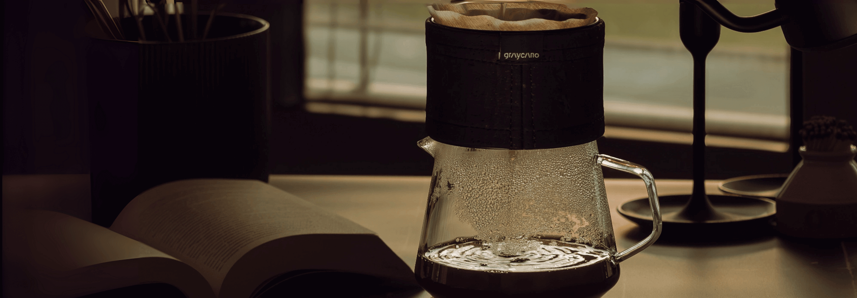 Pour-over coffee maker brewing on a desk beside an open book and a lamp, perfect for coffee enthusiasts.