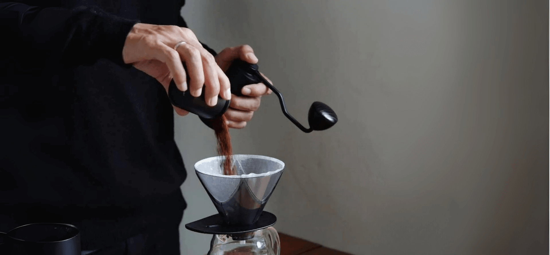 Hands pouring freshly ground coffee into a coffee filter for brewing, showcasing coffee preparation skills.