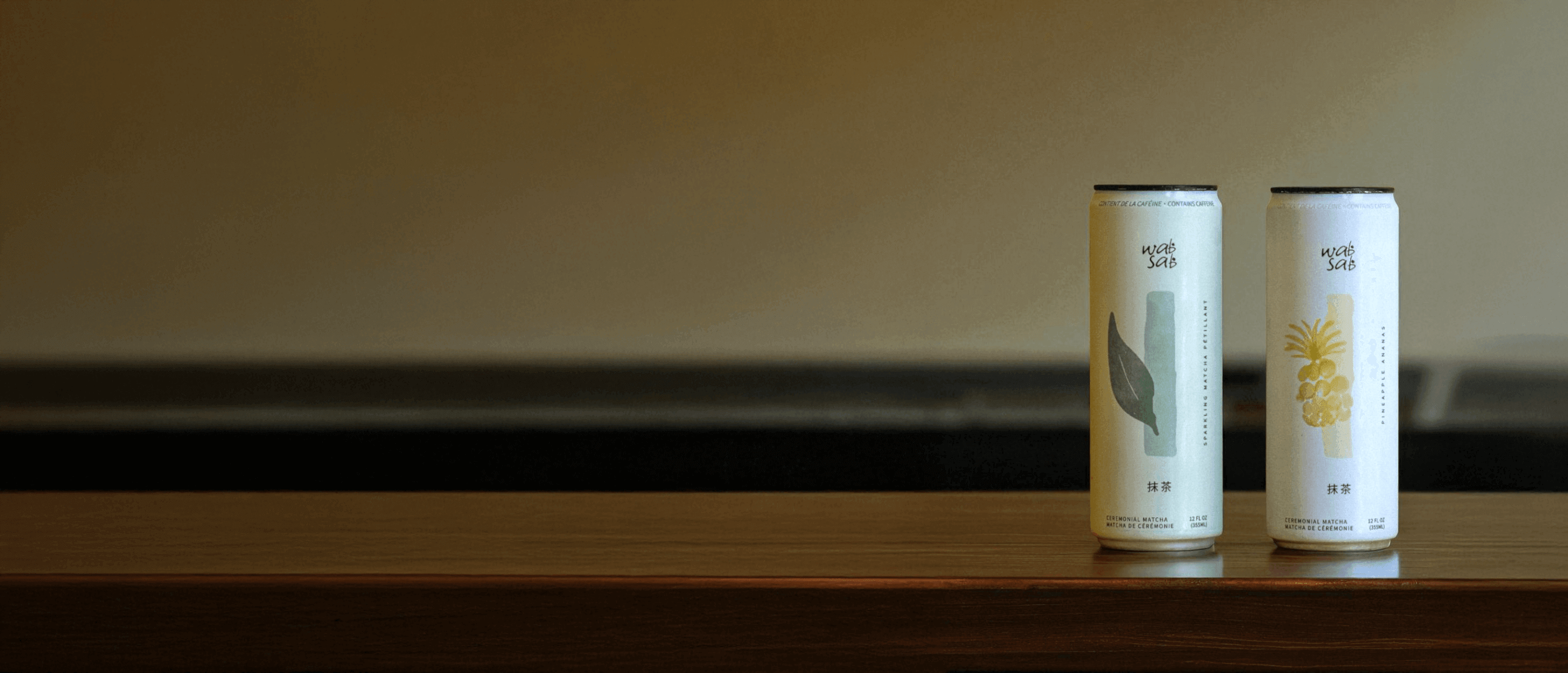 Two stylish beverage cans on a wooden counter, featuring natural leaf and pineapple designs, promoting a refreshing drink.