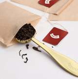 Biodegradable Tea Filters nestled with loose leaf tea in a golden spoon, promoting eco-friendly tea enjoyment.