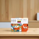 Drip box Columbia Decaf coffee package on a wooden table, showcasing vibrant design inspired by Colombian culture.