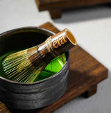 Era Dark Bamboo Chasen — Matcha Whisk immersed in matcha inside a ceramic bowl on a wooden surface.