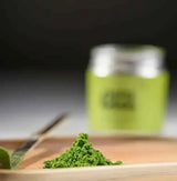 Era Dark Bamboo Chashaku — Matcha Spoon with matcha powder on a wooden tray and green jar in the background.