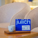 Blue coffee bag with 'julith' branding on a wooden coaster next to a white cup on a wooden table.