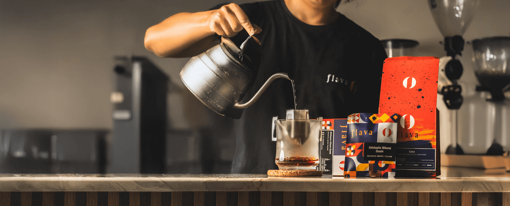 Barista pouring coffee with stylish equipment and colorful coffee boxes on the counter in a modern café.