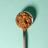 A stainless steel spoon filled with Mint Chocolate powder on a green background.