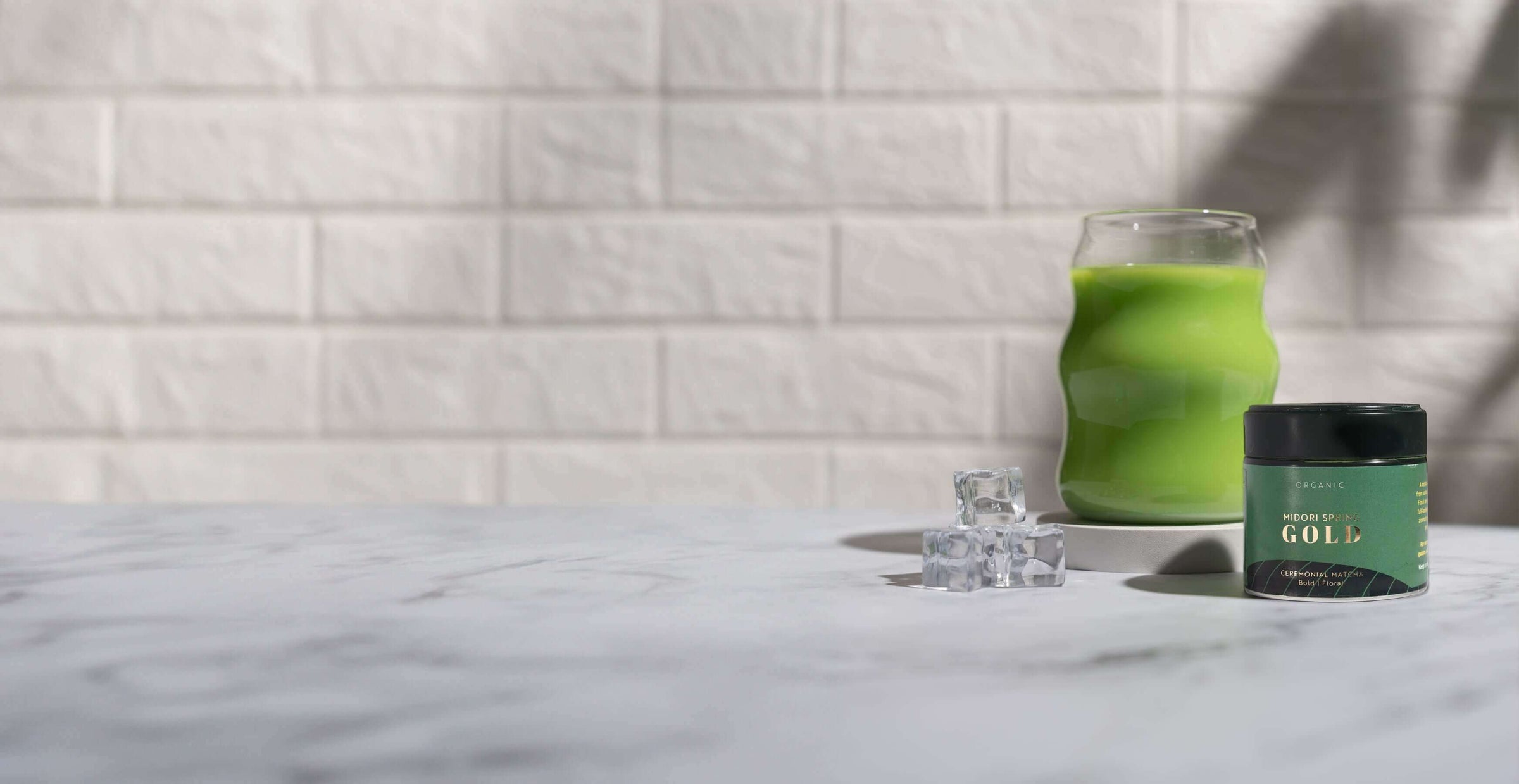 Green candle jar with matching green glass decor on marble surface against white brick wall