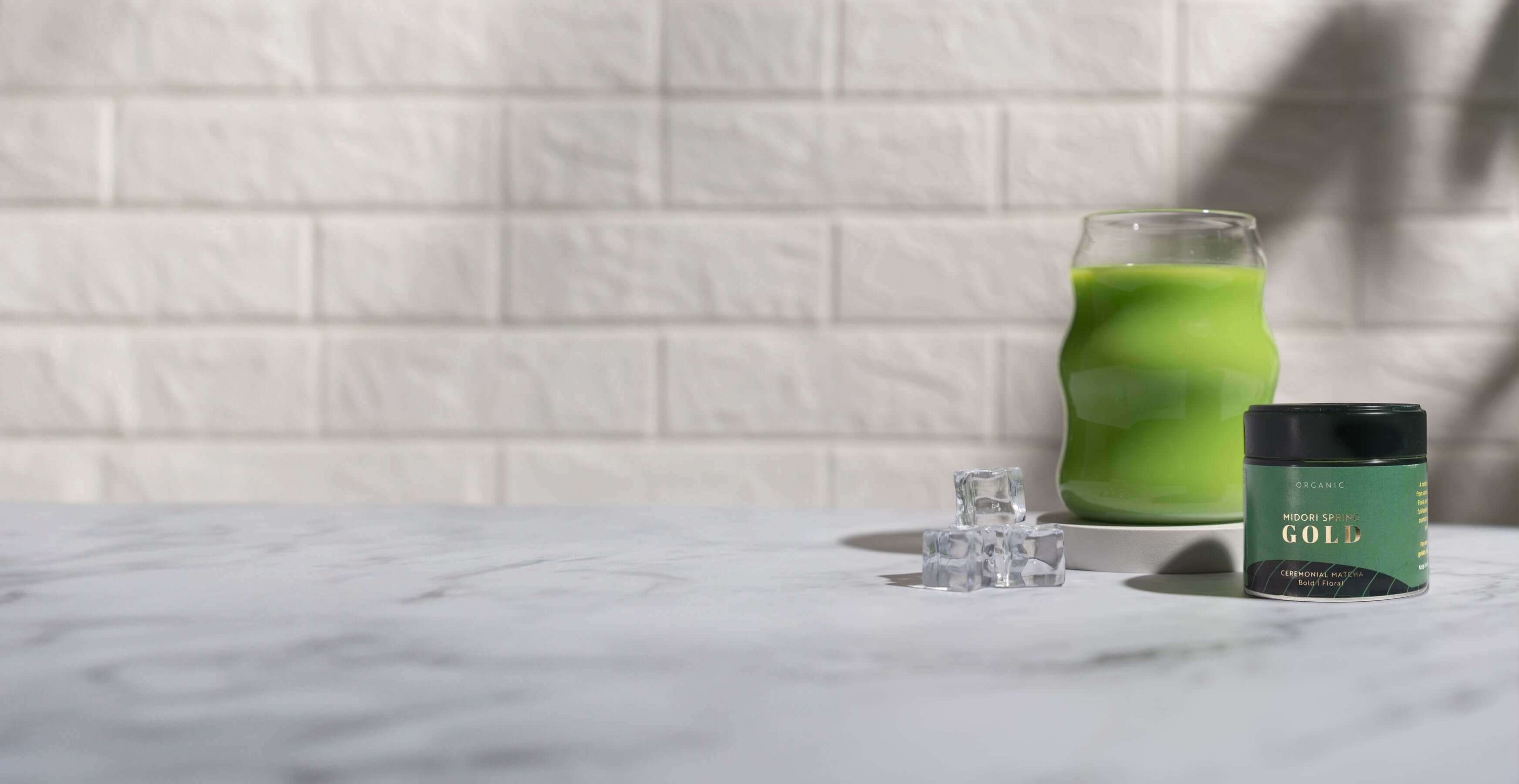 Green candle jar with matching green glass decor on marble surface against white brick wall