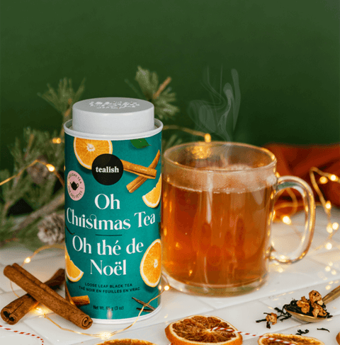 Festive Oh Christmas Blend tea canister beside a steaming cup, surrounded by holiday decorations and spices.