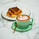 Cup of hot chocolate with latte art in green mug alongside a pastry
