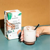 Box of Original Choc Blend with a glass of creamy chocolate drink and hand holding the glass.