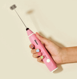 Hand holding a pink frother from The Pink Gift Set For Her, perfect for matcha and smoothie preparation.
