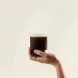 Chaga Mushroom Powder in a glass of dark wellness drink held by hand against a clean background