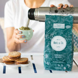 Pouring Pure Leaf Organic Yerba Mate from a stainless steel thermos into a light blue cup, with cookies in the foreground.