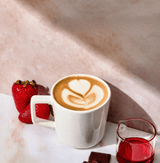 Delicious latte topped with creamy foam, fresh strawberries, and Strawberry Syrup on a marble surface.