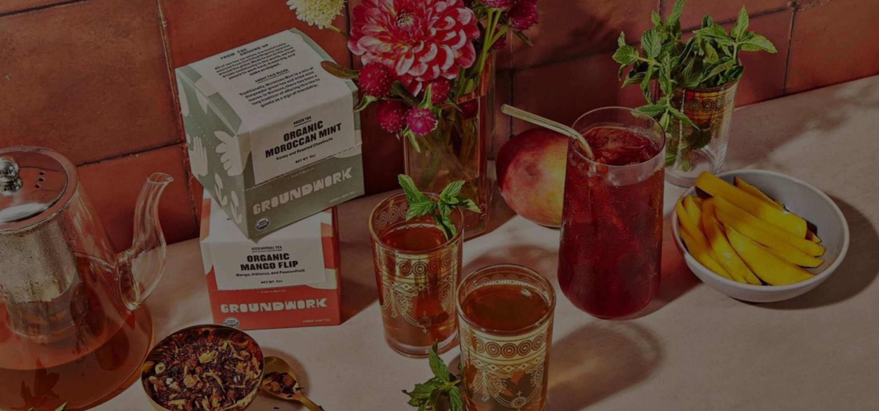 Organic boxed tea display with iced tea, fruit drinks, flowers, and a bowl of bananas on a table