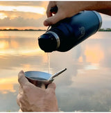 Yerba Mate Kit To Go portable thermos pouring mate into a gourd for outdoor brewing at sunset