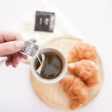 Yerba Mate Tea Bags being steeped in a cup next to croissants, showcasing an easy brewing experience.